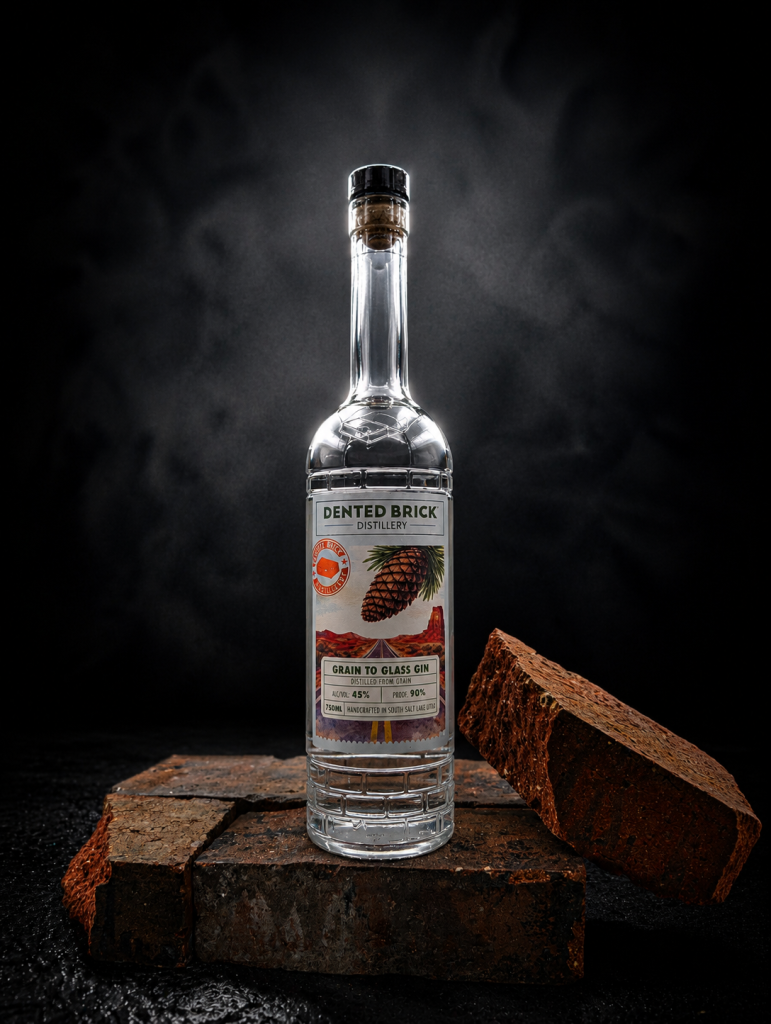 Bottle of Dented Brick Distillery Grain to Glass Gin on a stack of rough bricks against a dark background.