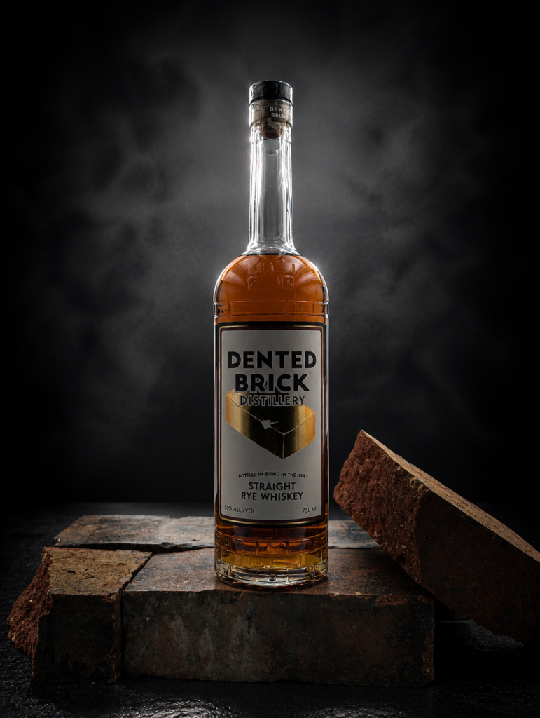 Bottle of Dented Brick Straight Rye Whiskey resting on stacked bricks against a dark studio background, label visible.