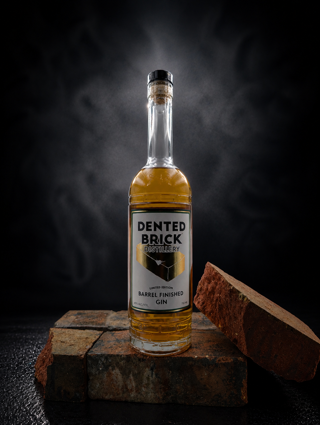 Dented Brick Distillery Barrel Finished Gin bottle centered on rustic brick blocks against a dark background, product shot.