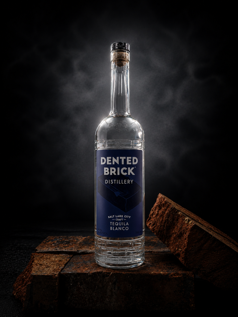 Dented Brick Distillery Tequila Blanco bottle standing on rough brick blocks against a dark smoky background