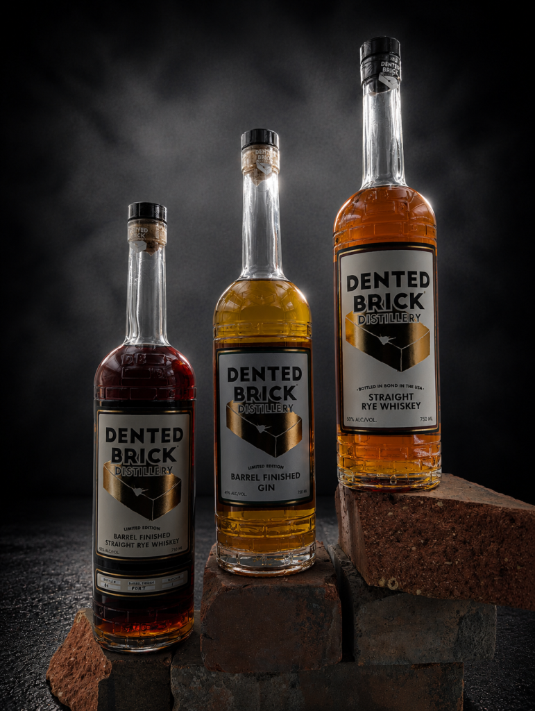 Three Dented Brick Distillery whiskey bottles on brick blocks against a dark backdrop, showcasing the three varieties.